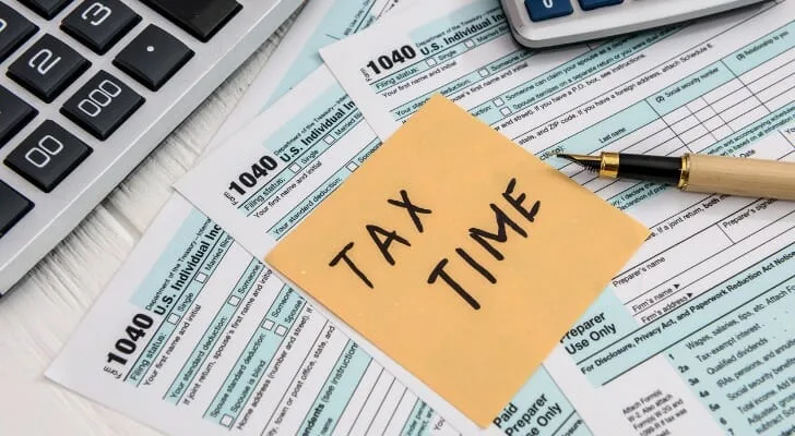 A &lsquo;Tax Time&rsquo; sticky note on 1040 forms with a pen and calculator